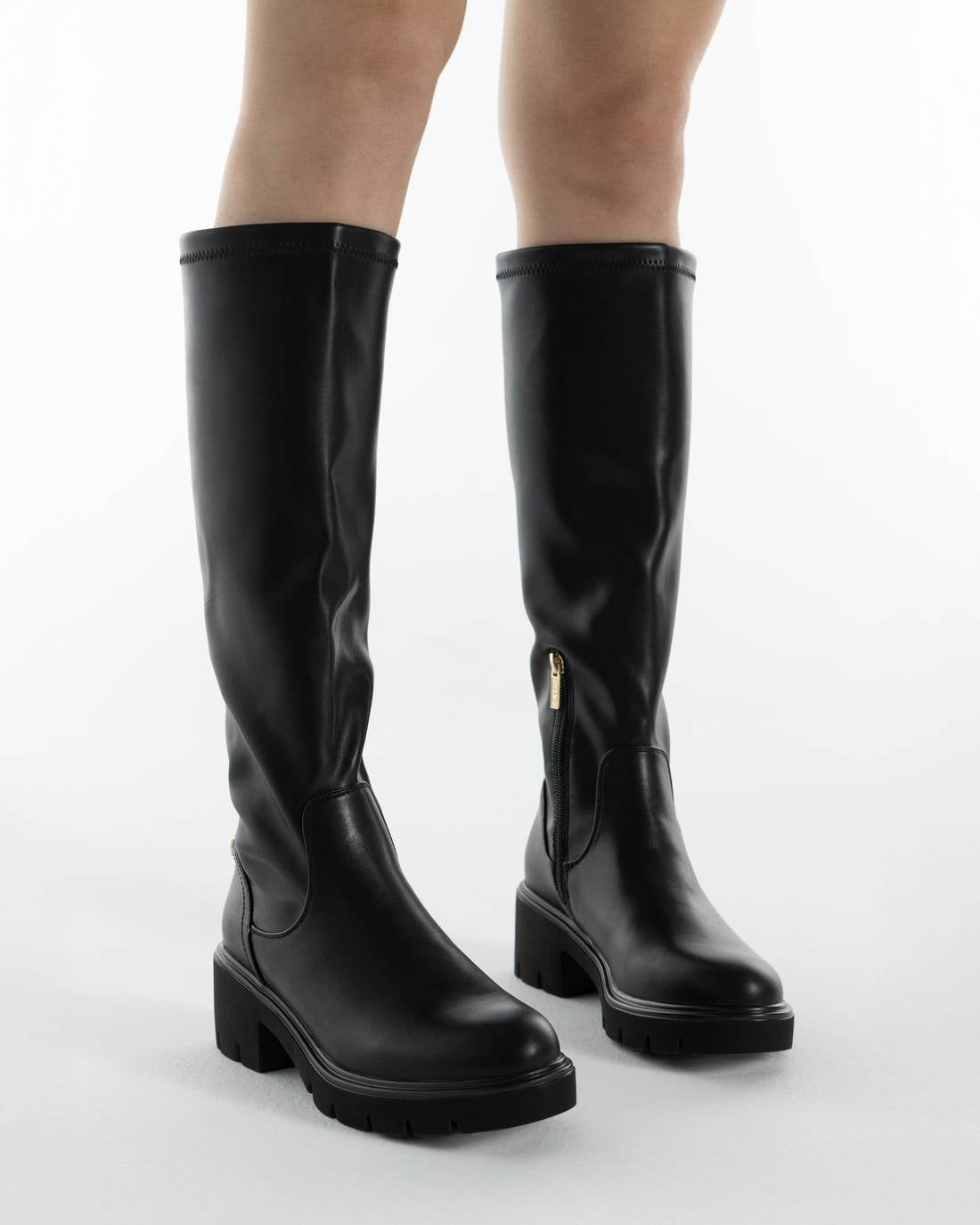 Pernas de mulher a usar bota XTi preta de cano alto com sola grossa