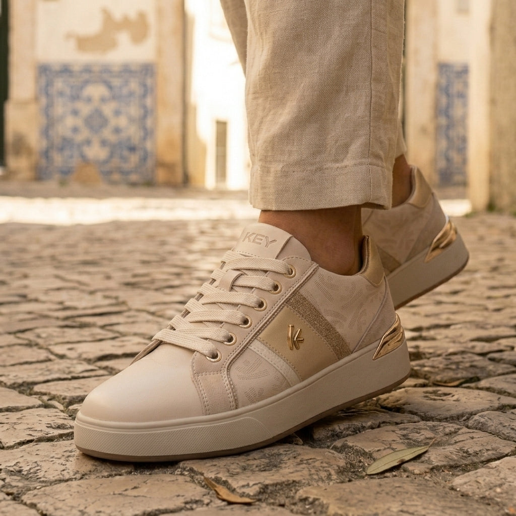 Pormenor dos pés a caminhar sobre calçada de pedra, com azulejos ao fundo, a usar as sapatilhas Keys 11870 Crema Cipria.