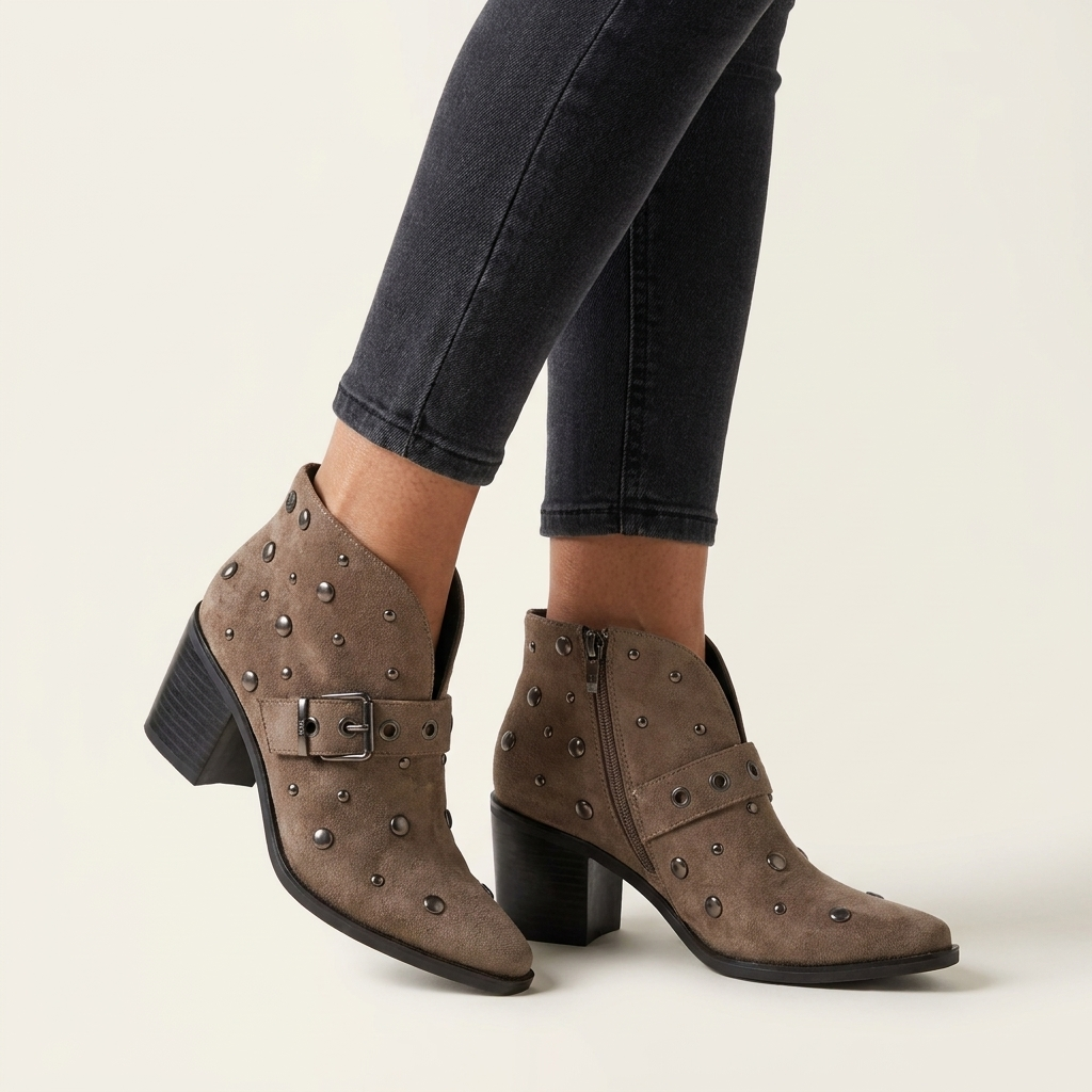 Botim XTi taupe em antelina com tachas e fivela lateral, calçado com calças pretas, em pormenor