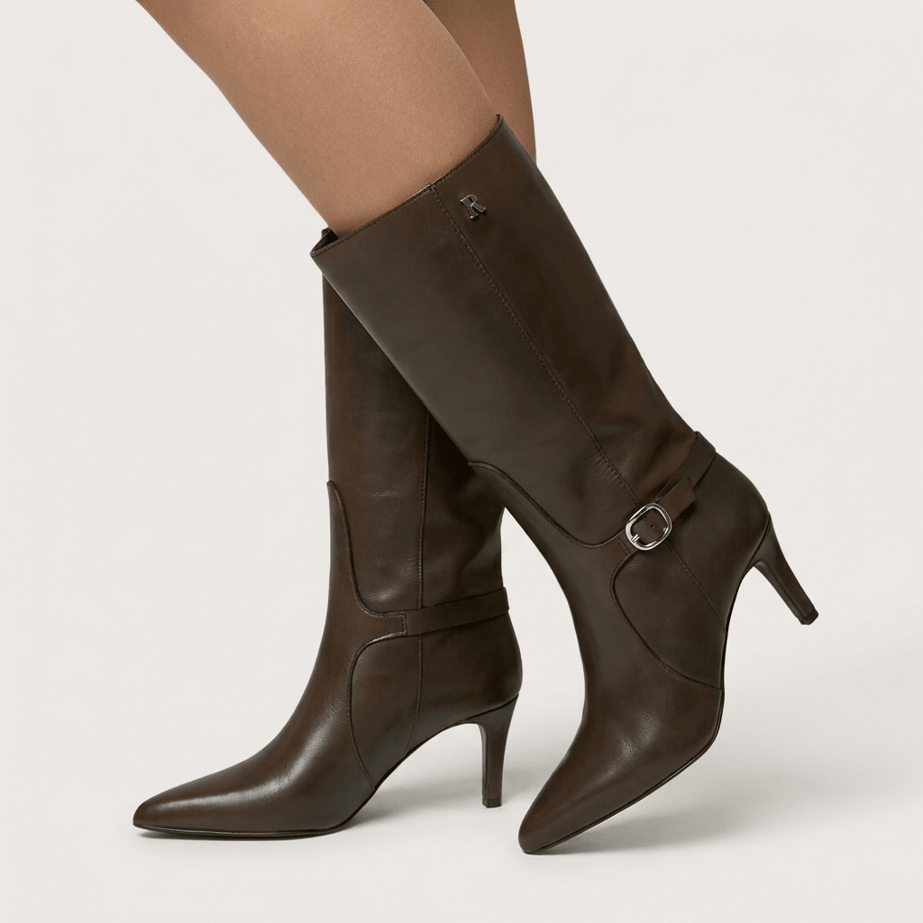 Detalhe das botas Ruika castanhas calçadas, com fivela lateral e salto fino, sobre fundo claro de estúdio
