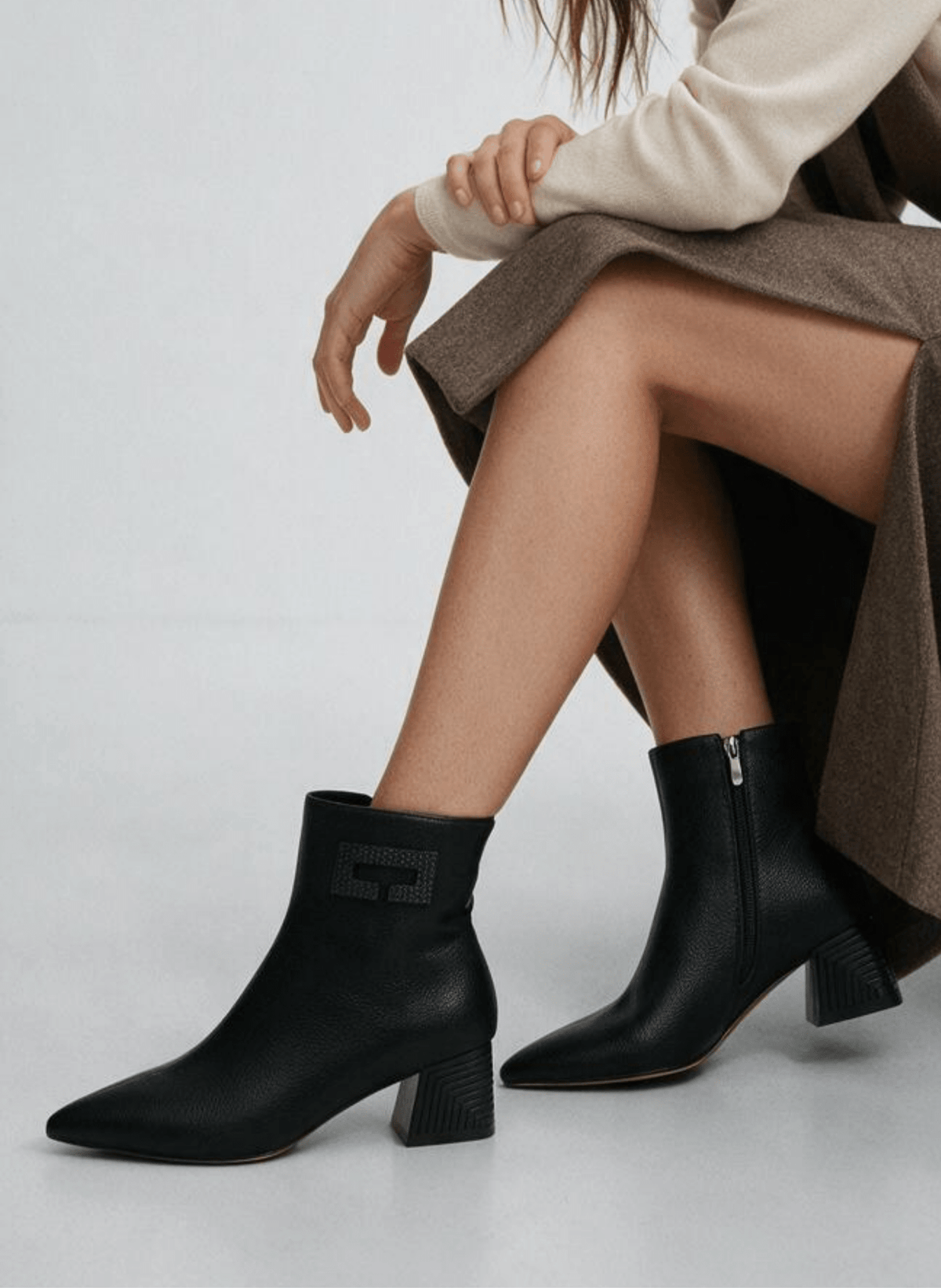 Mulher sentada com saia castanha, camisola creme e botins Azarey pretos de bico fino e salto geométrico