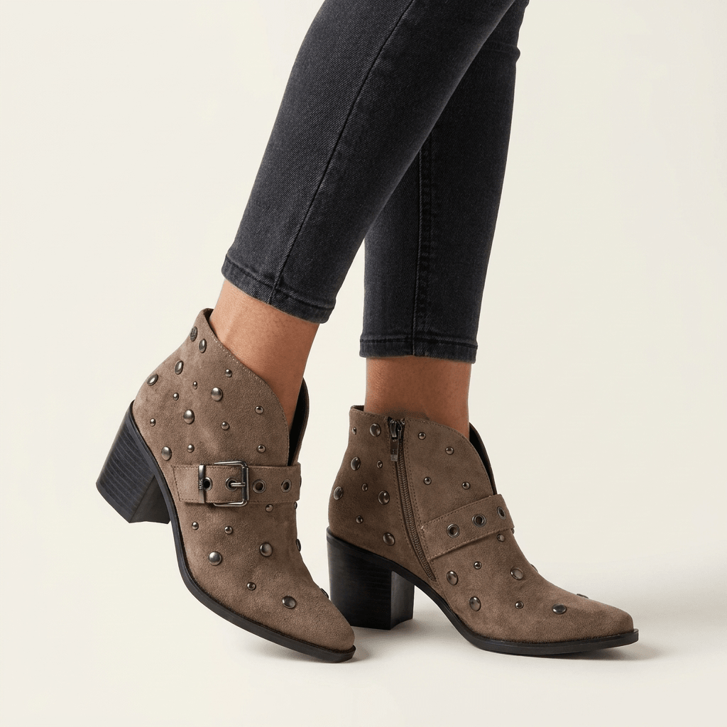 Botim XTi taupe em antelina com tachas e fivela lateral, calçado com calças pretas, em pormenor