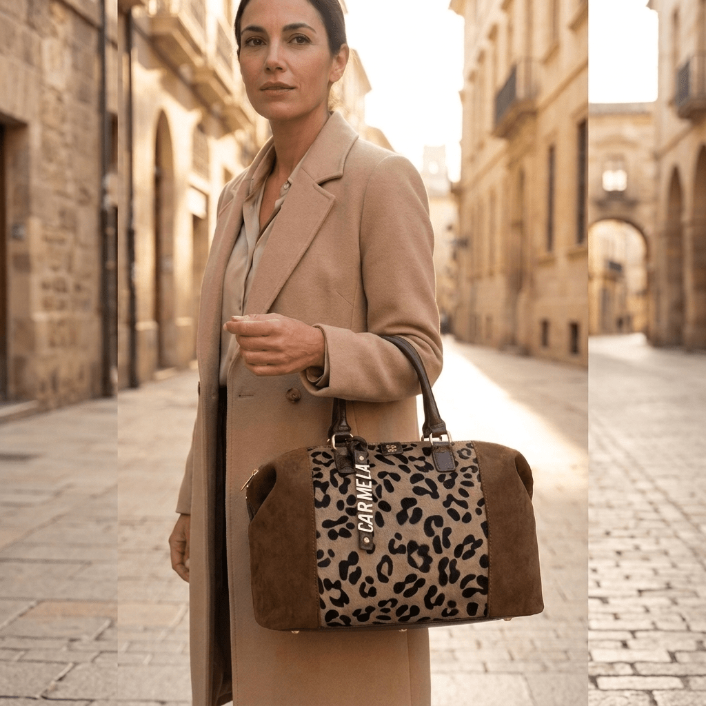 Mulher com casaco camel leva ao ombro a Mala Boston Carmela em animal print bege, numa rua de calçada portuguesa.