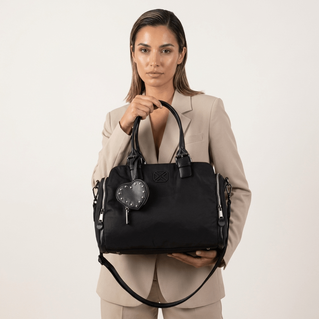 Mulher de blazer bege a segurar pelas pegas a mala de ombro Xti em têxtil preto, com porta-moedas em coração, em estúdio