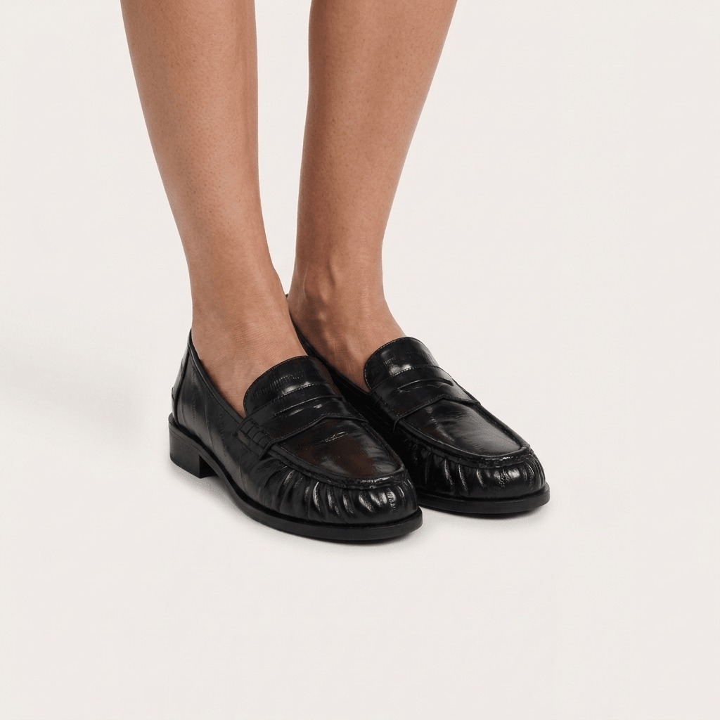 Pés de mulher com mocassins Xti pretos penny loafer, vista frontal sobre fundo claro