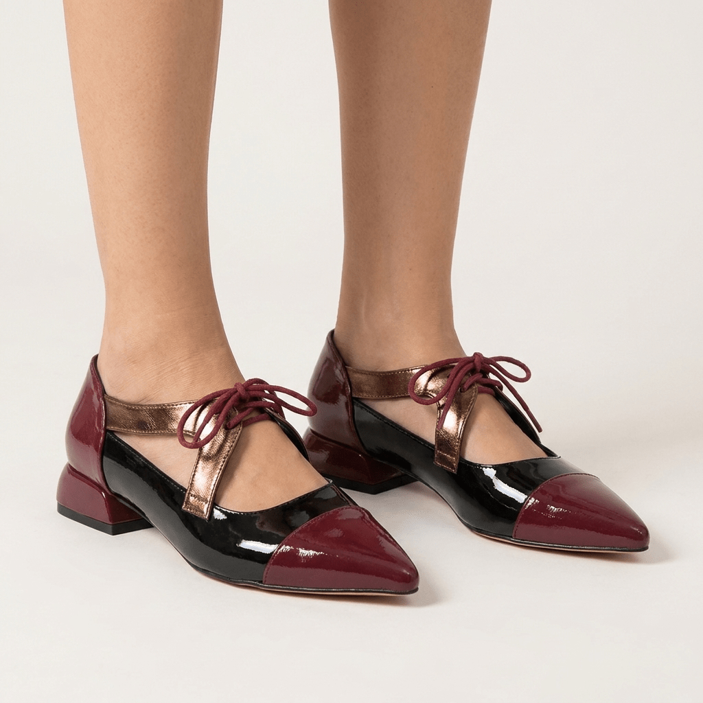 Par de sapatos Mary Jane Azarey bordeaux e preto nos pés, vista de três quartos, com tira cobre, cordões e tacão baixo, em fundo bege claro