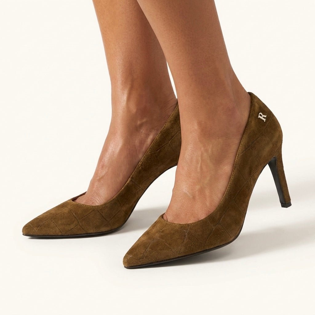 Pés de mulher a calçar sapatos Ruika em camurça camel texturada, de bico fino e salto fino, com logótipo R metálico na lateral