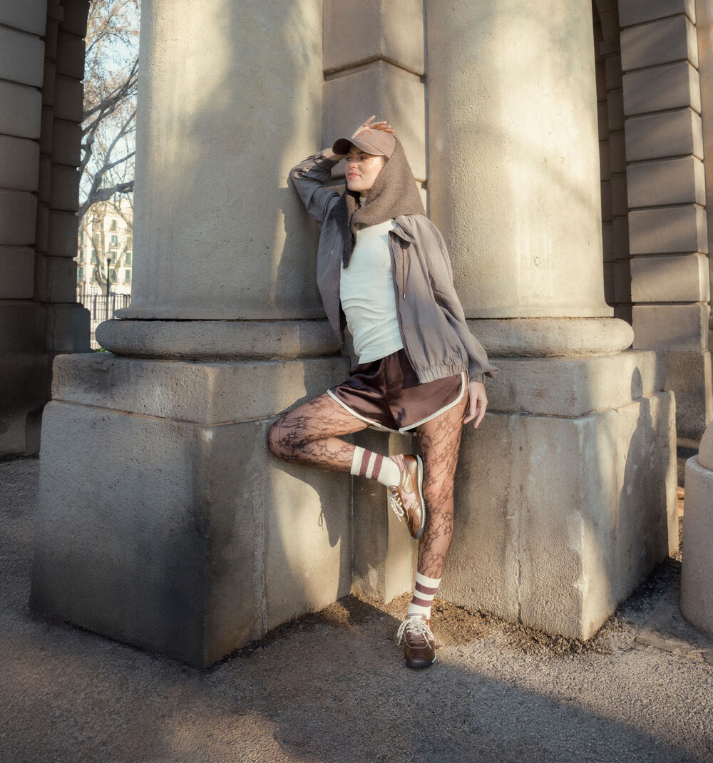Mulher com look outono-inverno, a usar as sapatilhas Victória Saturno junto a um monumento de pedra.
