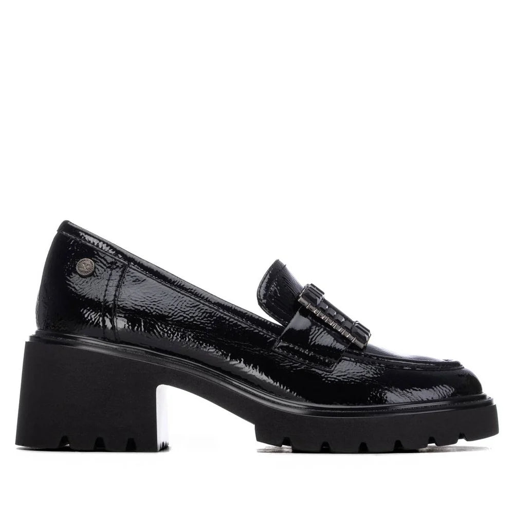 Mocassim feminino Xti em verniz preto, vista lateral de 3/4 mostrando o salto bloco de 7 cm e a fivela decorativa no peito do pé.