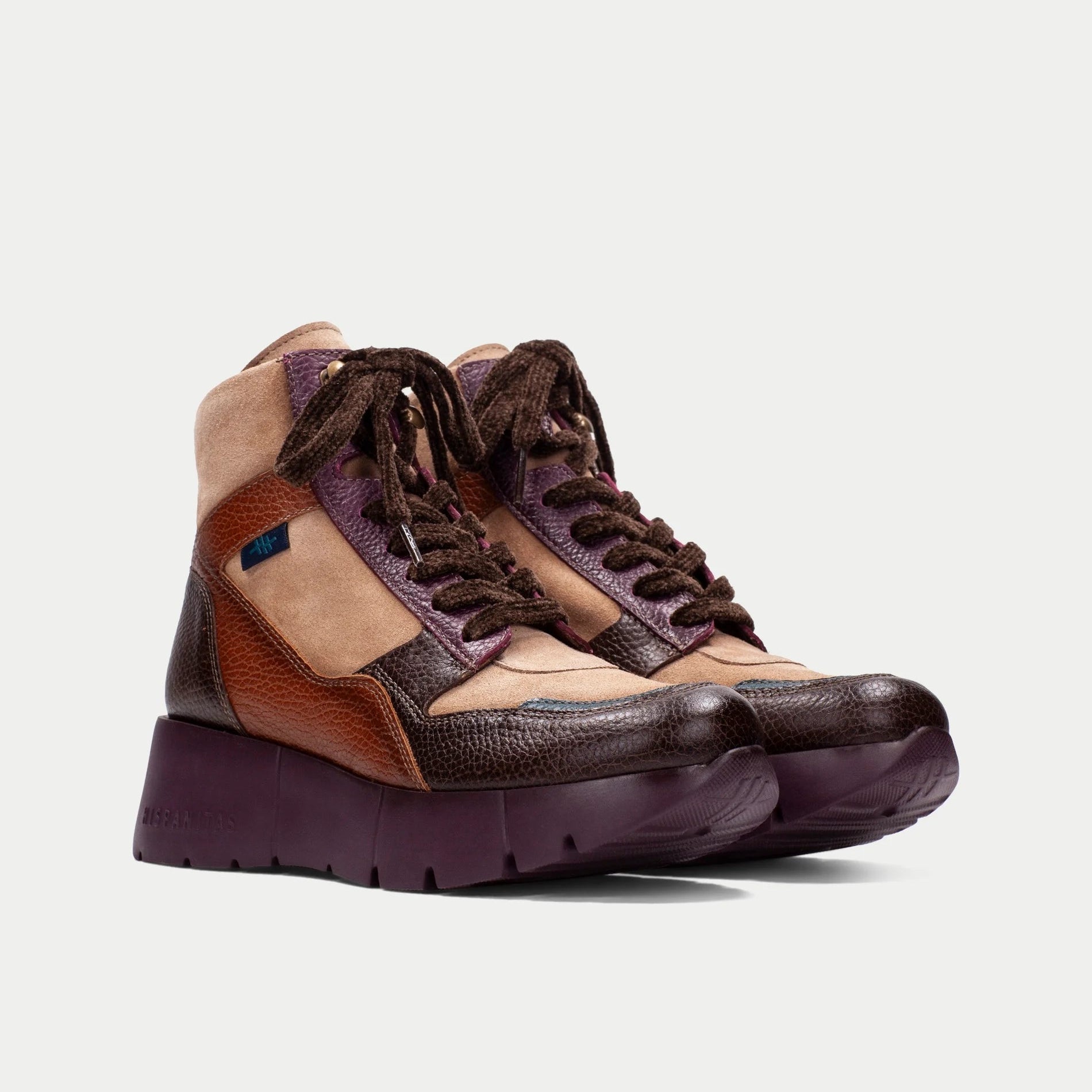 Par de botins Sport Hispanitas Chocolate-Amêndoa-Bordô fotografado em ângulo frontal ligeiramente lateral, em fundo neutro de estúdio, destacando os cordões em chenille castanho e a combinação de texturas camurça e couro.