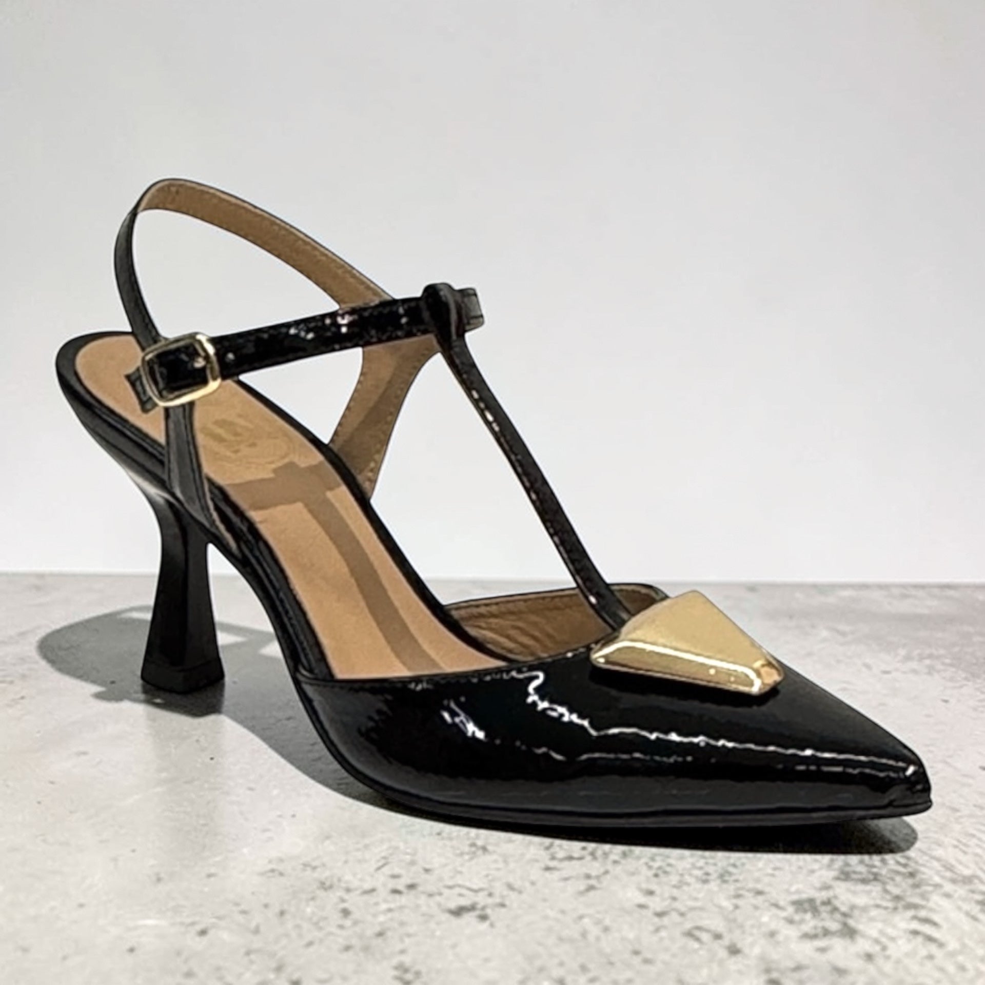Sapato feminino slingback em pele envernizada preta com tira em T, detalhe metálico dourado na biqueira e salto médio de 6cm.