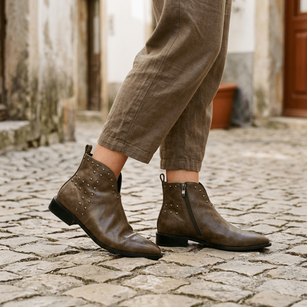 Botins Azarey taupe com tachas numa rua de pedra, com calças de linho