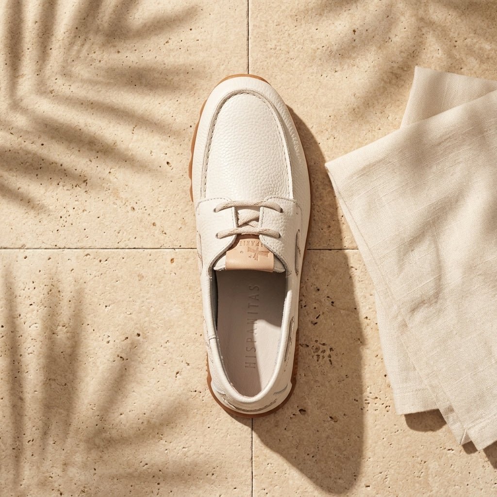 Mocassim Hispanitas Zinnia branco em still lifestyle, sobre piso em pedra com sombra de folhas e tecido em linho.