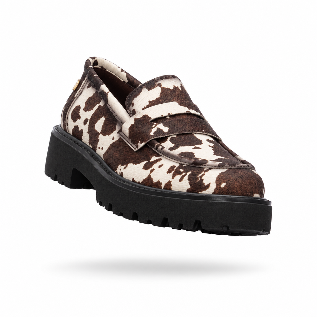 Mocassim Xti padrão vaca branco e castanho em levitação, vista três quartos frontal com sola tratorada preta, sobre fundo branco