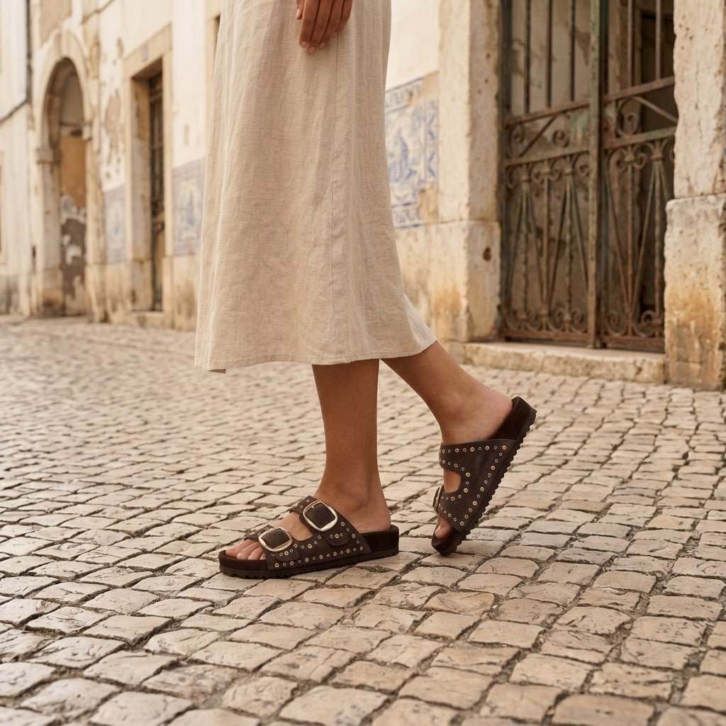 Mulher a caminhar em rua de calçada portuguesa, a usar sandália Xti castanha em camurça