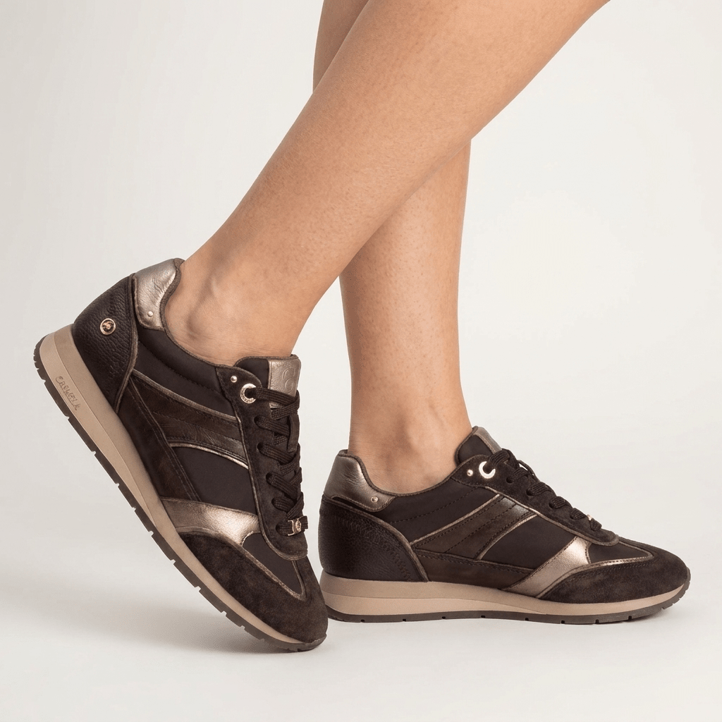 Pés femininos com sapatilhas Carmela castanho e bronze em movimento sobre fundo claro, com a sola jogging bege em destaque