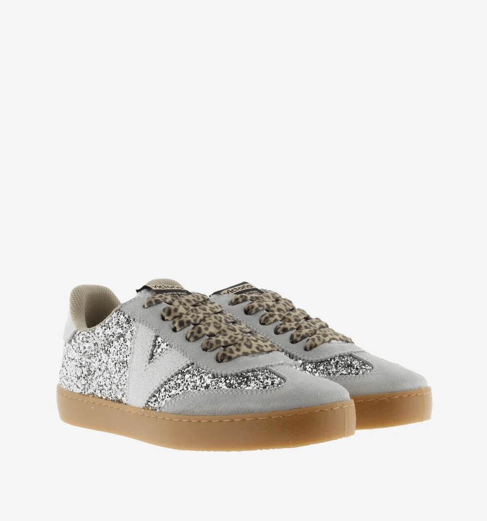 Par de ténis Victória glitter prateado com painéis em camurça cinza-clara, atacadores animal print, logotípo V branco, vista frontal em ângulo
