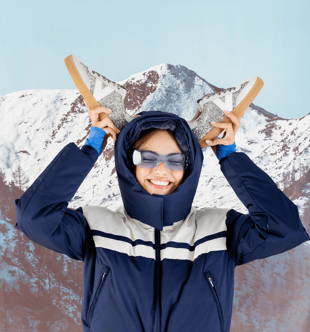 Ténis Victória glitter prateado segurados nas mãos por uma modelo com equipamento de esqui, fundo de montanha nevada, mostrando a sola caramelo