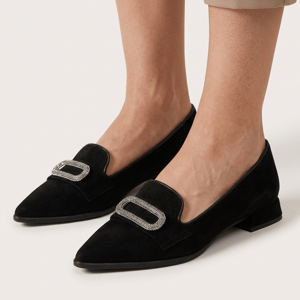 Pormenor frontal de pés com sapatos Turtle de camurça preta, bico fino e aplicação decorativa prateada com textura, sobre fundo claro